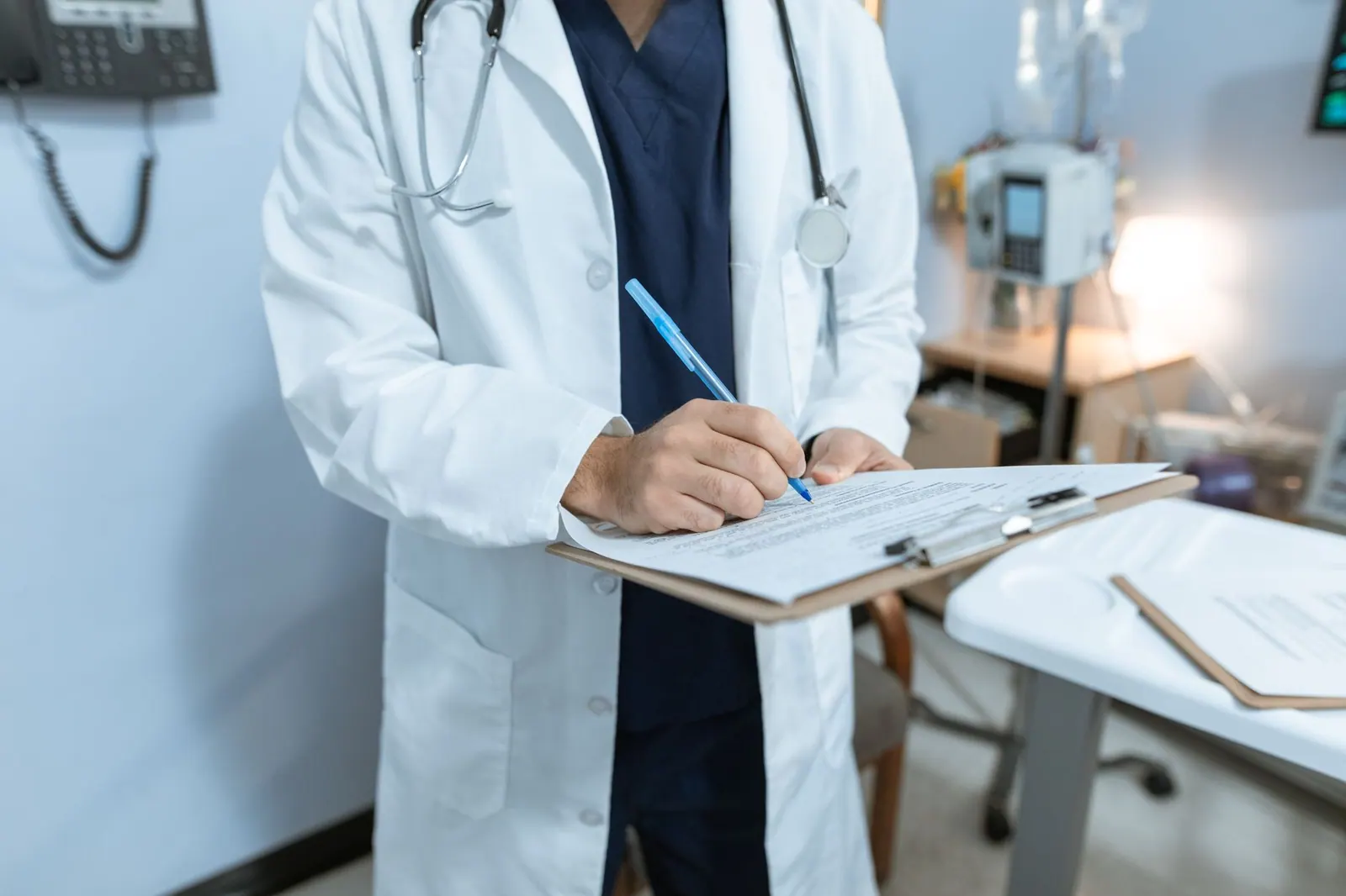 A doctor in a lab coat writing notes in a hospital setting, using a clipboard. Healthcare Reputation Management Guide for 2027