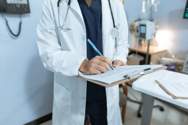 A doctor in a lab coat writing notes in a hospital setting, using a clipboard. Healthcare Reputation Management Guide for 2027