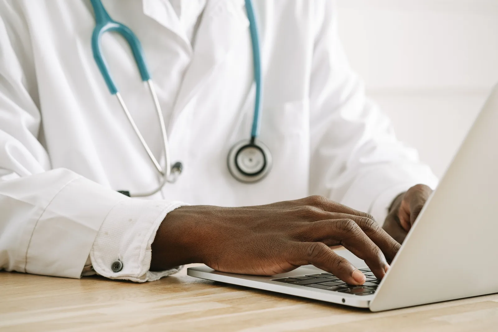 Close-up of a doctor using a laptop, wearing a stethoscope and white coat. Healthcare Reputation Management Tools: How to Vet Them Before Signing