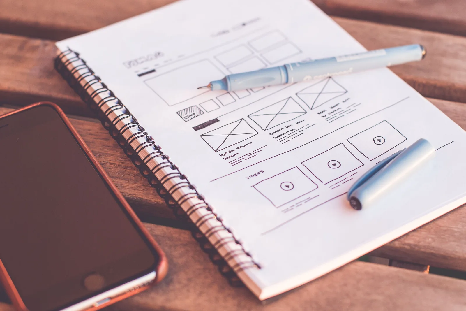 Close-up of a notebook with wireframe sketches and a smartphone on a wooden desk. Healthcare SEO Page Designs Worth Copying for Every Service Line