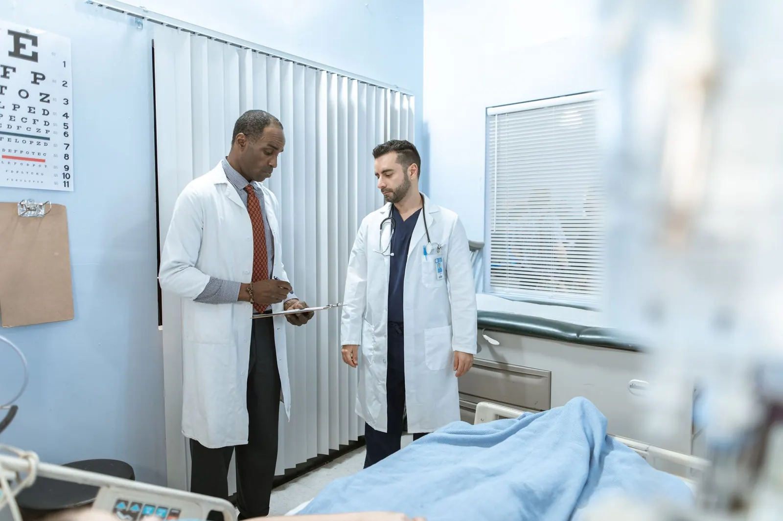 Two doctors review a patient's chart in a hospital room, focusing on healthcare cooperation and medical care. 5 Patient Outreach Metrics That Flag Problems Before Patients Leave