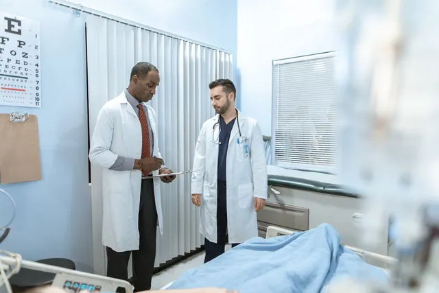 Two doctors review a patient's chart in a hospital room, focusing on healthcare cooperation and medical care. 5 Patient Outreach Metrics That Flag Problems Before Patients Leave