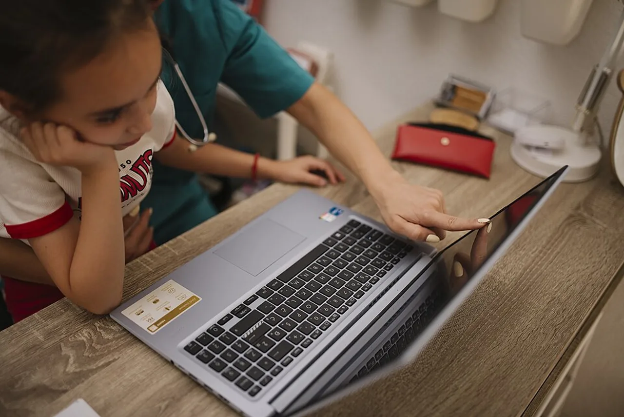 A child and a healthcare professional look at information on a laptop in a medical office.