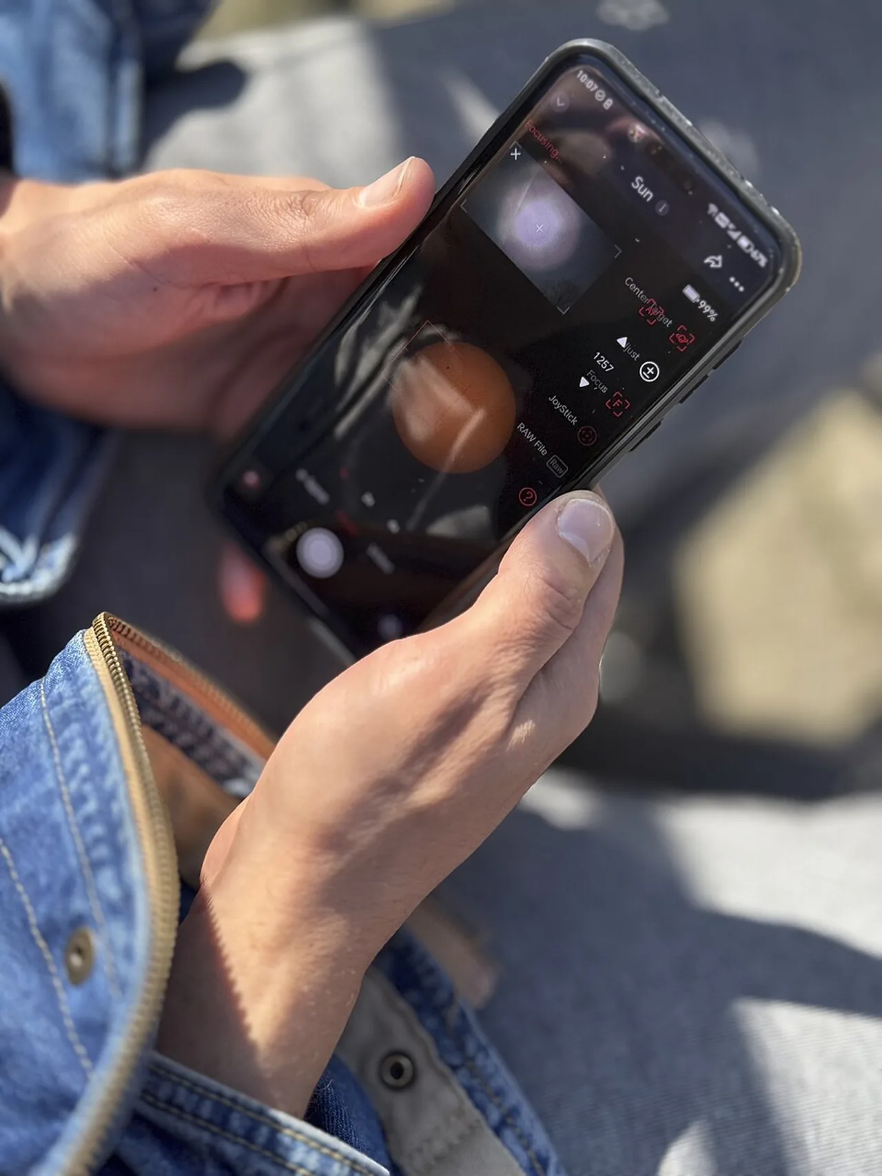 A person holds a smartphone with the camera application open while sitting outdoors.