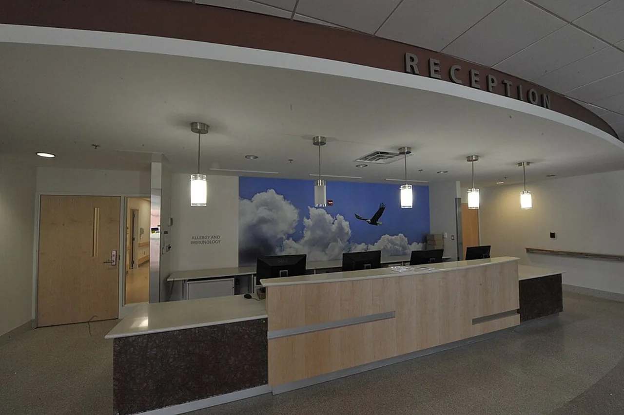 An unoccupied hospital clinic reception desk stands beneath a large reception sign.