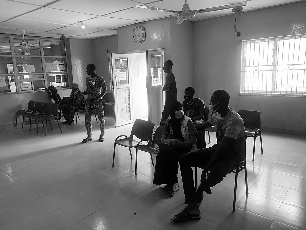 People wait on spaced chairs inside a health center reception area.